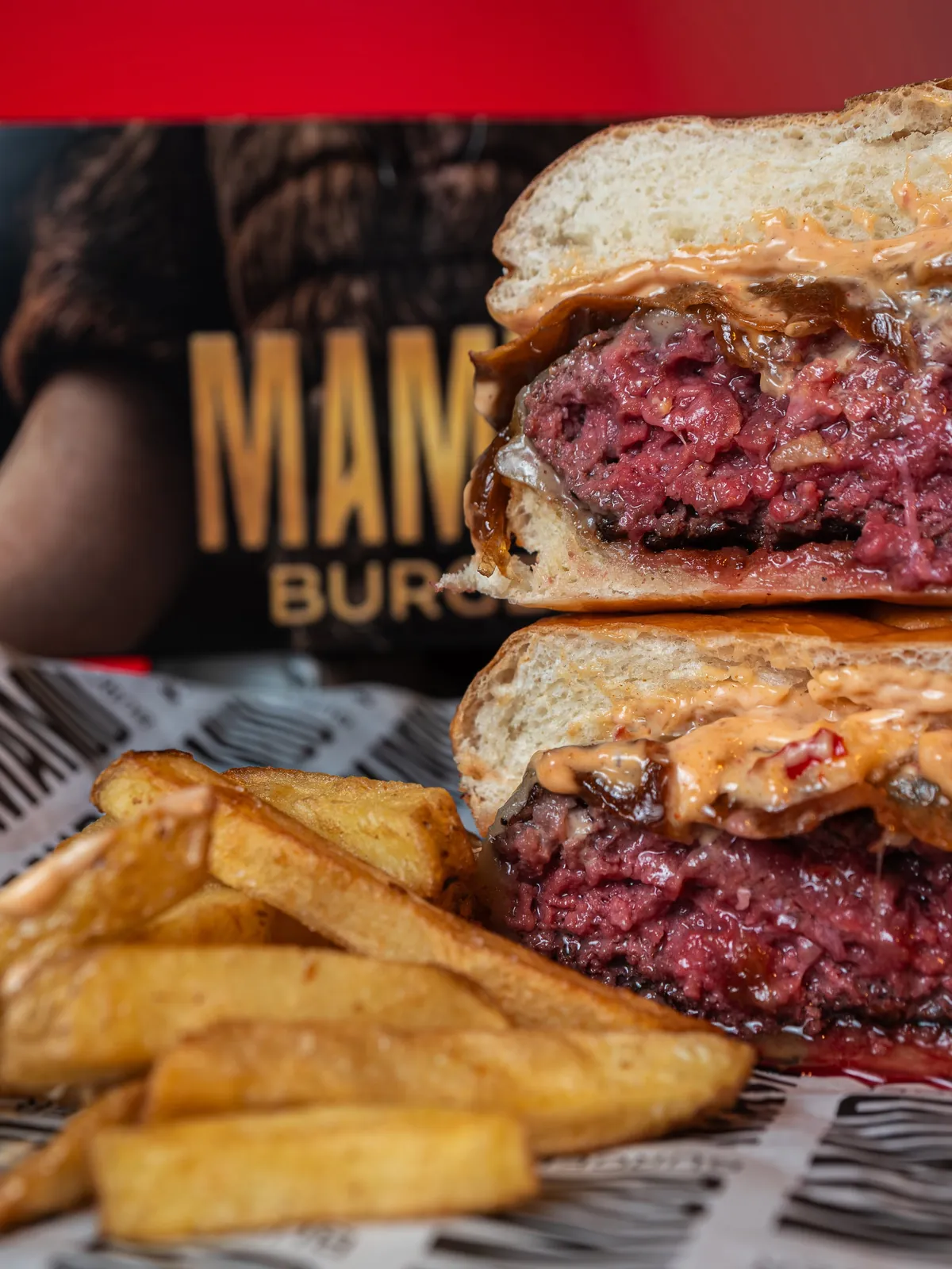 Burger de Mamud cortada por la mitad junto a papas fritas y la caja de Mamud Burger
