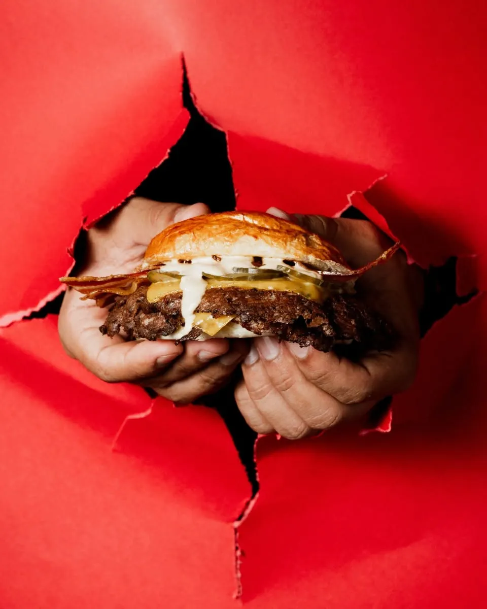 Manos sacando una burger a través de un papel rojo rasgado