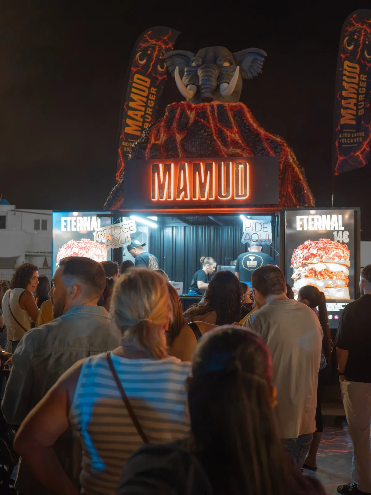 Stand de Mamud Burger con el mamut sobre el volcán iluminado, de noche, en el Burger Fest Canarias